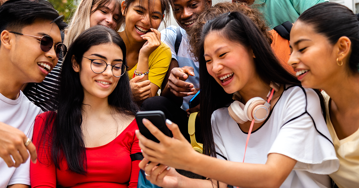 Group of smiling teenagers sharing a smartphone, highlighting peer connection and adolescent emotional well-being.